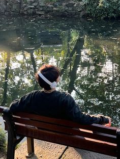 a woman sitting on top of a wooden bench next to a river filled with water