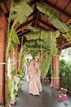 a woman in a pink sari walking down a walkway with greenery on either side