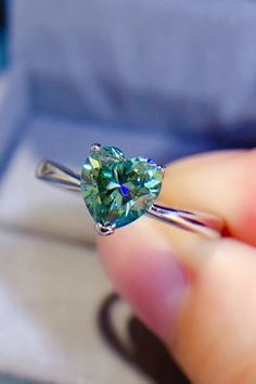 a person holding a ring with a heart shaped green diamond in it's middle