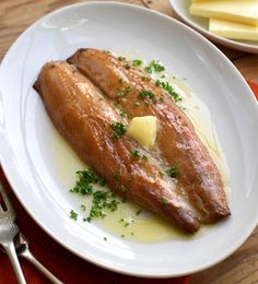 two pieces of fish on a plate with butter and parsley