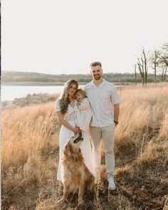 a man and woman standing next to a brown dog on top of a dry grass field