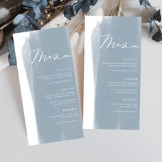 two folded menus sitting on top of a table next to some flowers and feathers