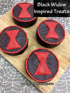 four black and red decorated cookies sitting on top of a cutting board with the words black widow inspired treats