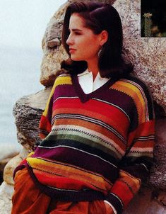 a woman is sitting on the rocks wearing a colorful sweater and orange pants with her hands in her pockets