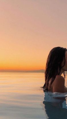 a woman is sitting in the water and kissing her man's forehead with an orange sunset behind her