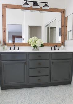 a bathroom vanity with two sinks and a large mirror above it, in front of a floral arrangement on the counter