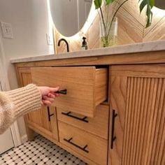 a person is opening the door to a bathroom vanity with wooden drawers and black handles