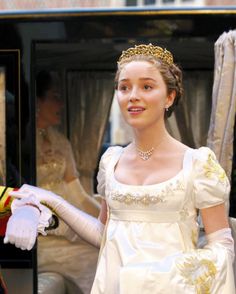 a woman in a white dress and gold tiara standing next to a man in a red suit