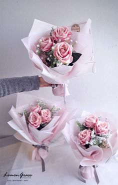 three bouquets of pink roses are being held by someone's hand in front of a white wall