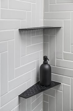 a black bottle sitting on top of a shelf next to a white tiled bathroom wall