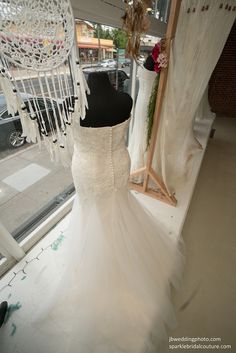 a wedding dress on display in front of a window with other dresses hanging from it