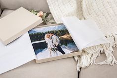 an open box with a photo on it next to a white blanket and flower bouquet