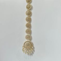 a gold necklace with several circular designs and pearls hanging from it's side on a white background