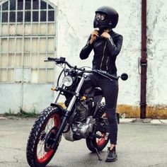 a woman in black is standing next to a motorcycle and talking on her cell phone