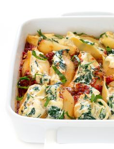 a white casserole dish filled with pasta and spinach covered in sauces