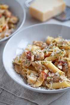 two bowls filled with pasta and meat on top of a white cloth next to cheese