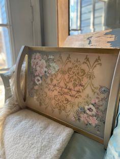 a wooden frame with flowers on it sitting next to a white towel and window sill