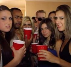 a group of people standing around each other holding red cups