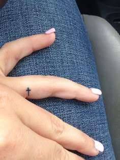 a person with pink fingernails and a cross tattoo on their finger, sitting in a car