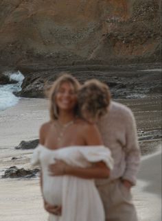 two people are hugging on the beach by the water's edge, with waves crashing in to shore behind them