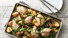 a pan filled with chicken and green beans on top of a wooden table next to a plate