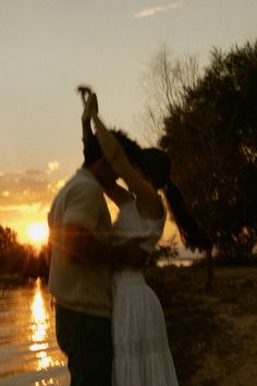 a man and woman standing next to each other in front of the water at sunset