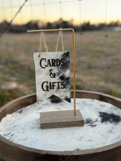 a sign that says cards and gifts hanging from a wooden stand on a barrel in the grass