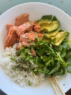 a white bowl filled with rice, meat and veggies next to chopsticks