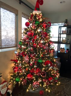 a decorated christmas tree in a living room with red and green ornaments on the top