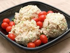 a black plate topped with chicken salad and cherry tomatoes on top of a pink napkin