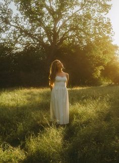 a woman in a white dress is standing in the grass with her head turned to the side