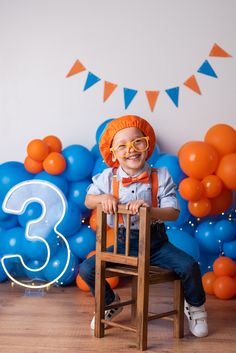 a young boy sitting on a chair in front of balloons and garlands for his 3rd birthday