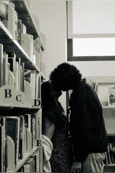 a man and woman kissing in front of bookshelves