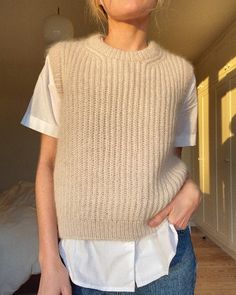 a woman standing in front of a bed wearing a sweater