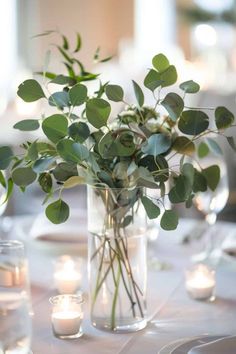 a vase filled with lots of greenery on top of a table next to candles