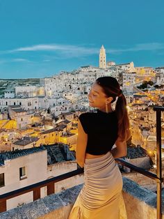 a woman standing on top of a roof looking at the city below her and smiling