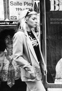 black and white photograph of a woman walking down the street in front of a store