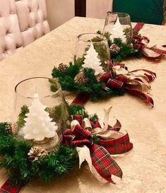 two glass vases sitting on top of a table covered in bows and pine cones