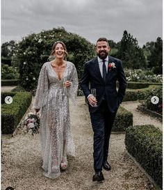 a man and woman in formal wear walking down a path with flowers on either side