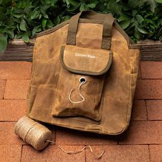 a brown bag sitting on top of a brick floor next to a spool of thread