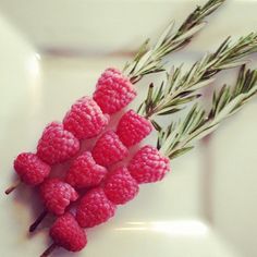 raspberries are arranged on a white plate with rosemary sprigs in the center