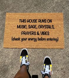 someone standing in front of a door mat that says, this house runs on music, sage crystals, prayer & vibes look your energy before entering