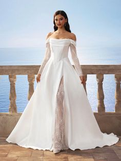 a woman in a white wedding dress standing on a balcony with the ocean behind her