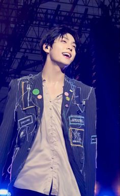 a male in a black and white jacket is smiling at the camera while standing on stage