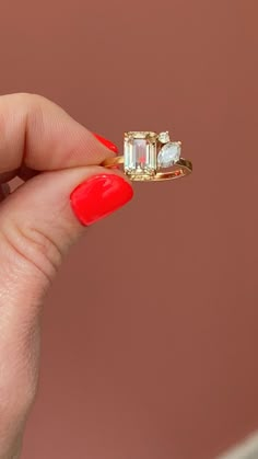 a woman's hand holding an engagement ring with two diamonds on it and red nail polish