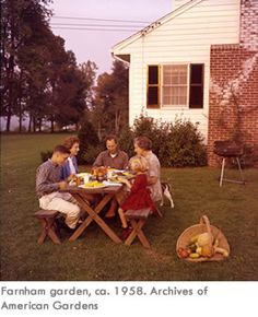 a group of people sitting around a table eating food in front of a white house