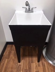 a white sink sitting on top of a wooden floor next to a metal trash can