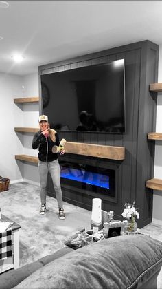 a woman standing in front of a fireplace with a tv on it's wall