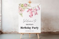 a welcome sign for a baby shower with pink flowers and clothes hanging on a line