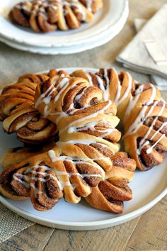 several cinnamon buns with icing on a white plate next to two silver plates